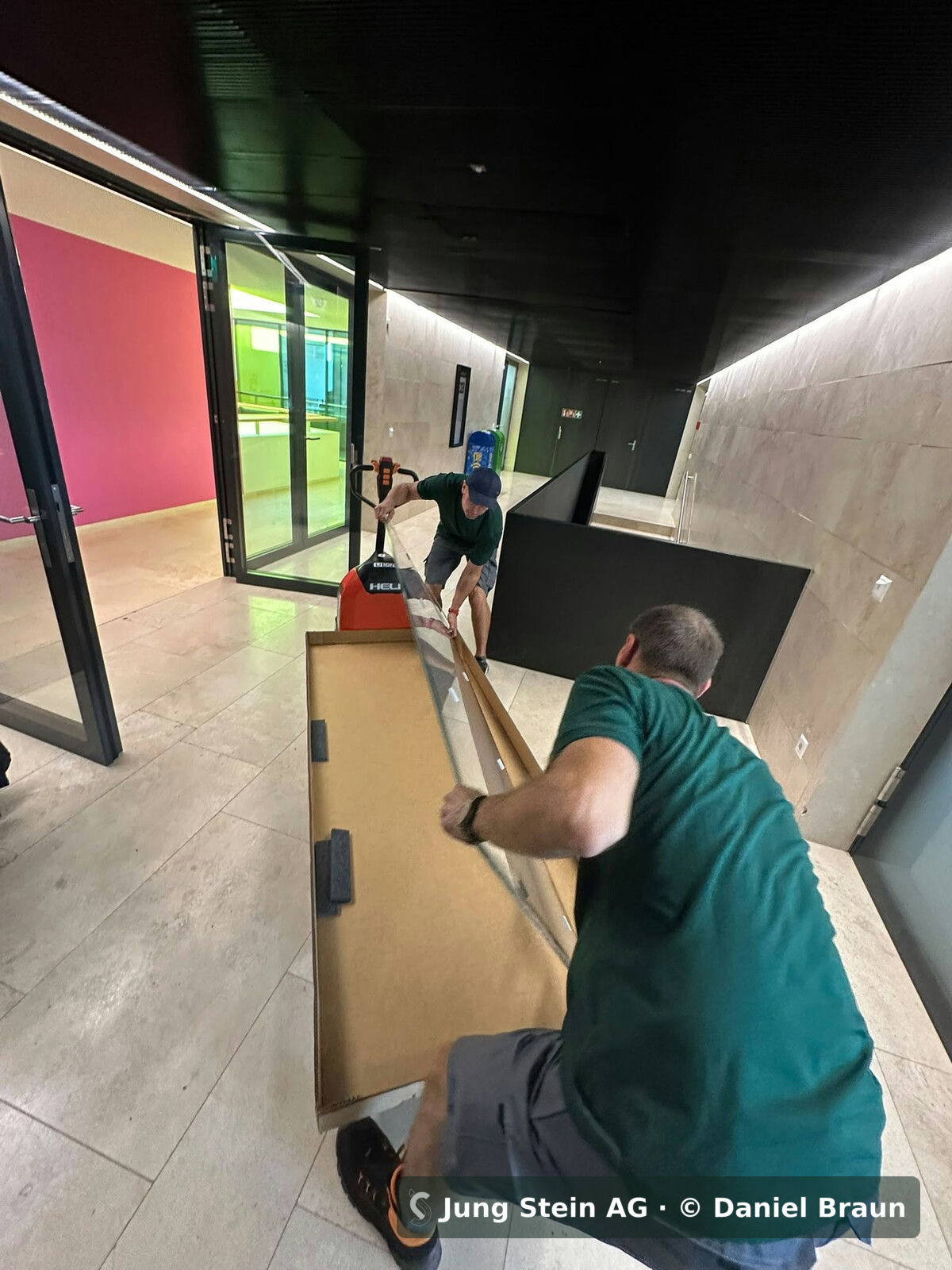 Büromontage auf einem Hochschulcampus in Zürich: Transport eines grossformatigen Glaselements zu zweit durch das Gebäude – Jung Stein AG für die Weber Büro AG
